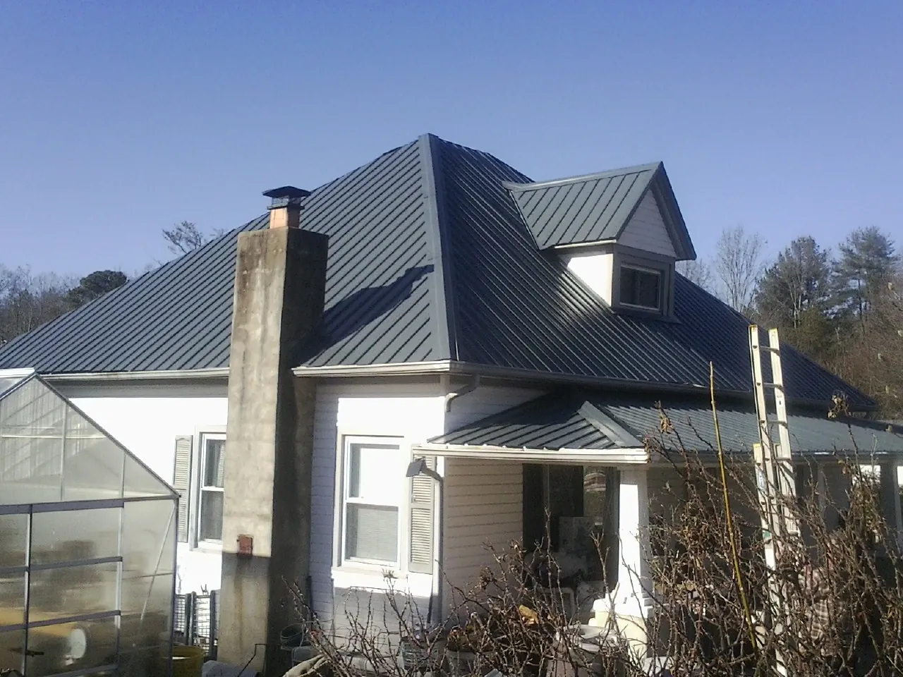 Dark blue standing seam metal roof on a white farmhouse with dormer — Slate & Tile Roof Repair by Roofing Brothers in Clear Lake