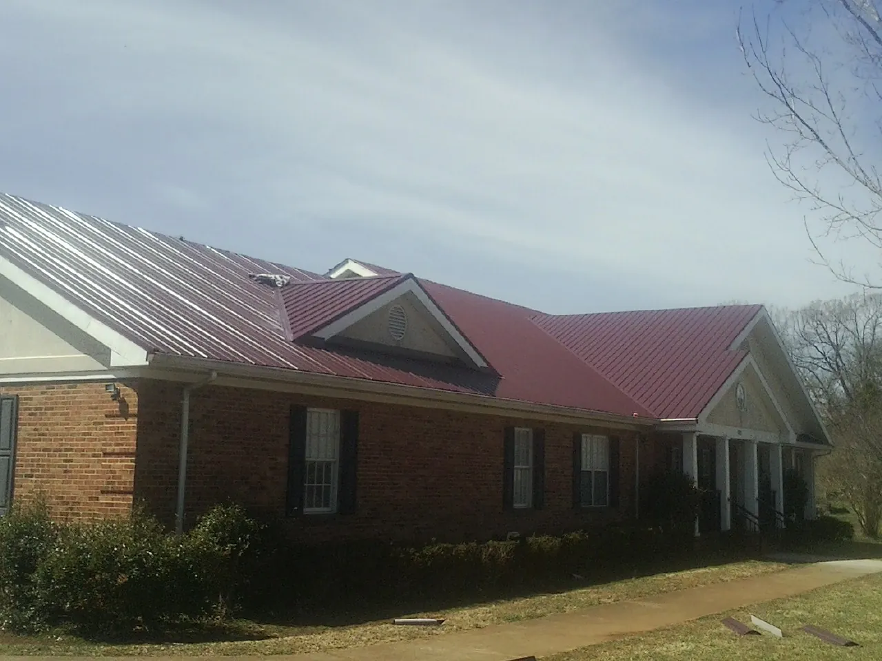Red metal roof with gabled entries on a long brick building, from a Hail Damage Roof Repair job in Clear Lake