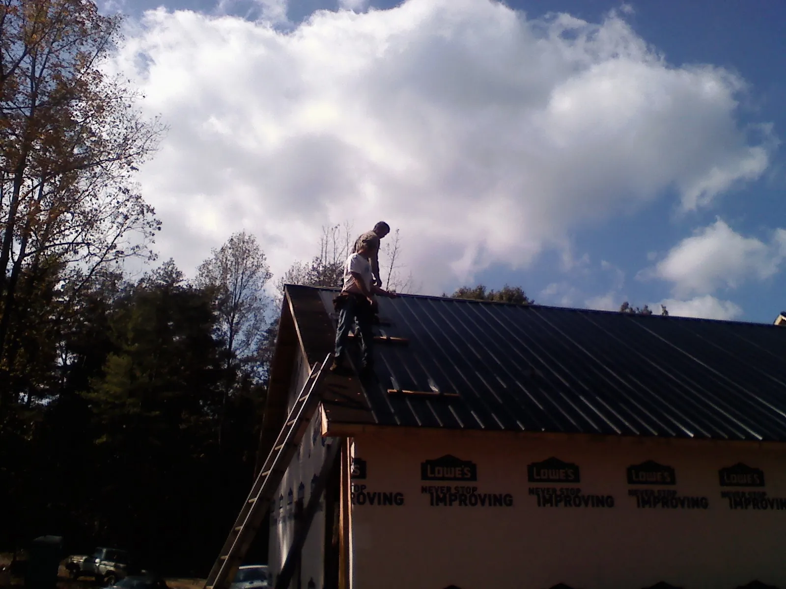 Roofer fastening dark metal panels high against a cloudy sky, from a Roof Inspection job in Clear Lake