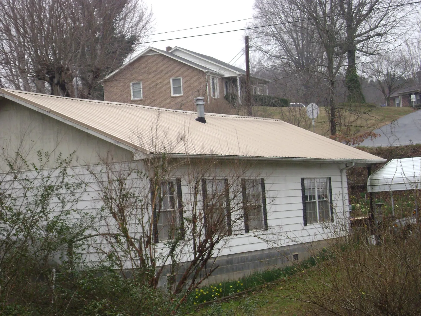 Tan metal roof on a white sided house set into a hillside — Commercial Roofing by Roofing Brothers in Clear Lake